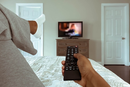 Woman Lounges in Bed Watching TV