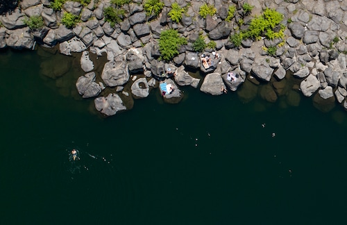 An overhead view of the Clackamas River and its rocky shore as people swim and sunbathe in the area