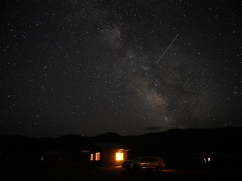 stars and milky way over a small wooden cabin at night