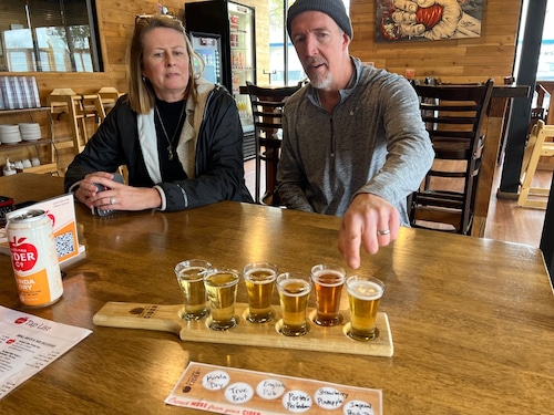 A man and a woman sit in from of a taster tray of ciders.