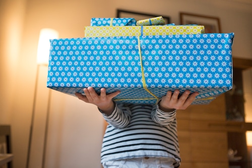 Child carrying several gifts wrapped in blue and yellow paper and tied with paper ribbon